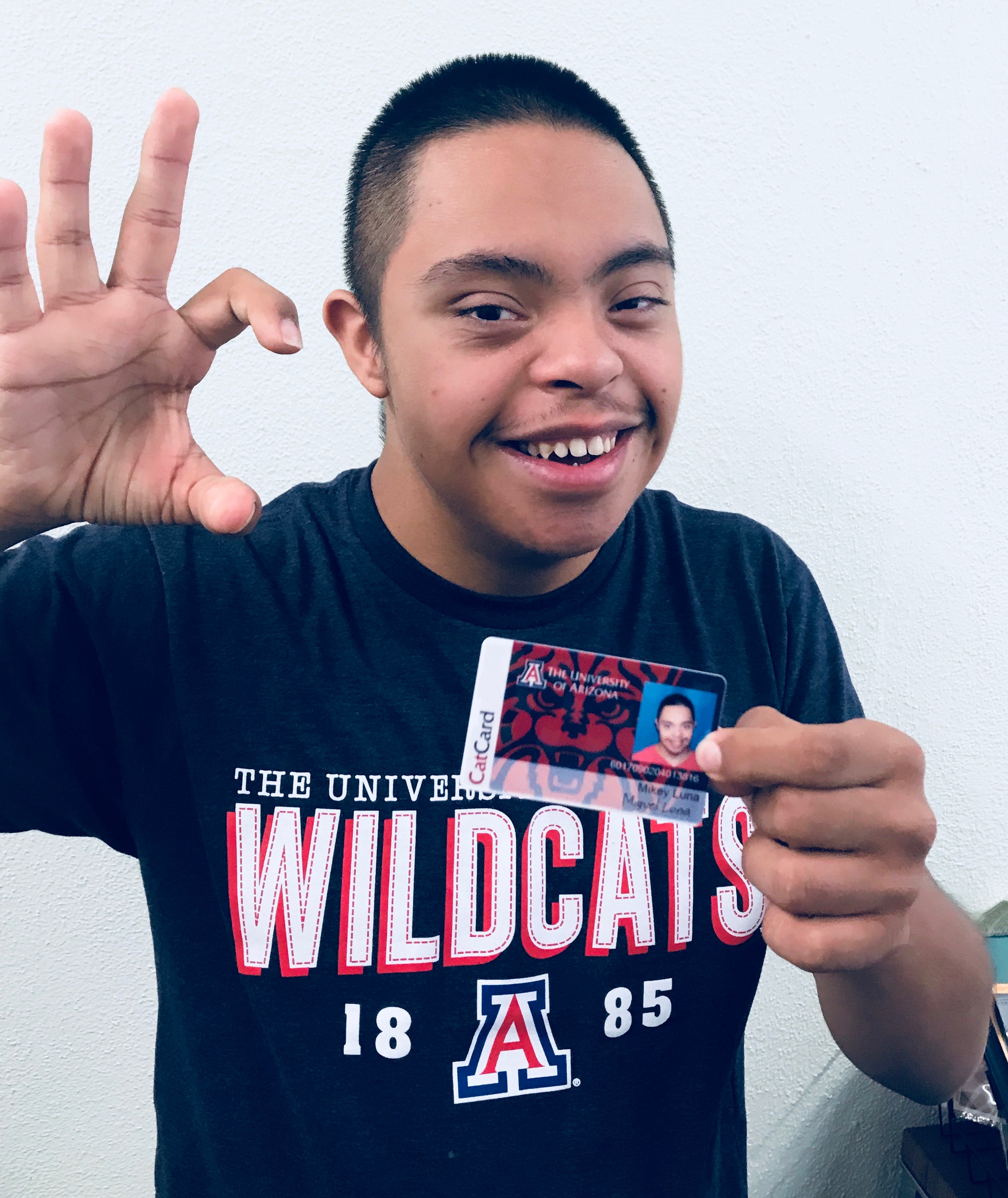 student holding cat card and making wildcat symbol with hand