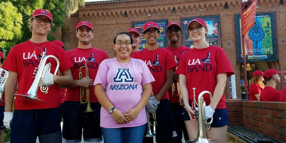 female student posing with UArizona marching band during pep rally