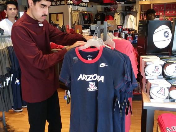 A student working at the UArizona bookstore with a peer mentor looking on as support