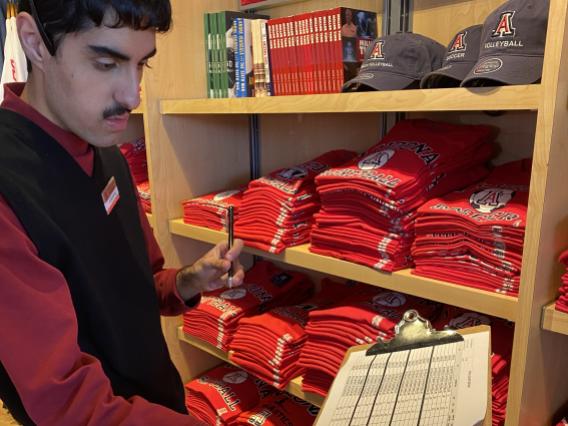 male student taking merchandise inventory at McKale Center bookstore