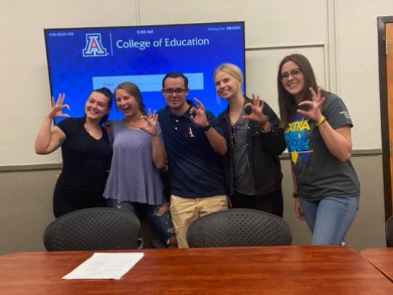 group of students standing in front of conference room smiliing with wildcat sign