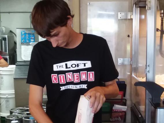 male student is filling popcorn bags with popcorn at movie theater