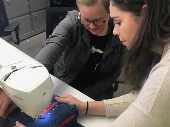 two students using sewing machine during design class