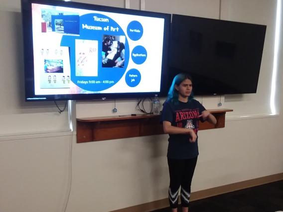 female student standing in front of IEP presentation signing as she leads the meeting