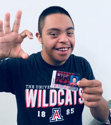 student holding cat card and making wildcat symbol with hand